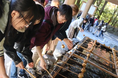 手水舎で手の清め方を説明する学生