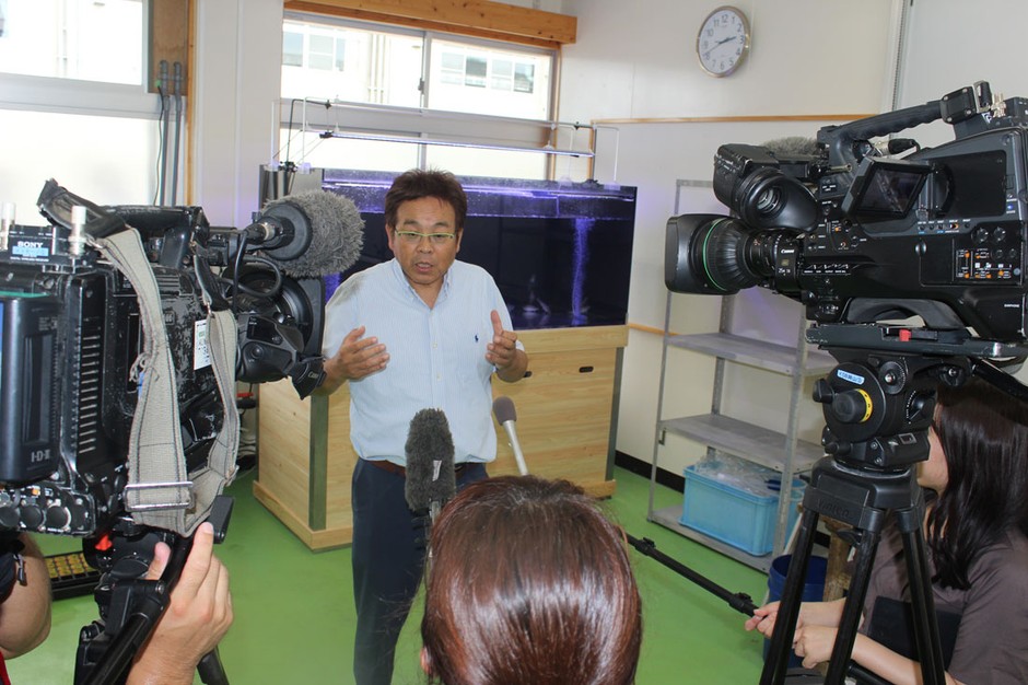 大型水槽前で報道陣の取材に答える山本准教授