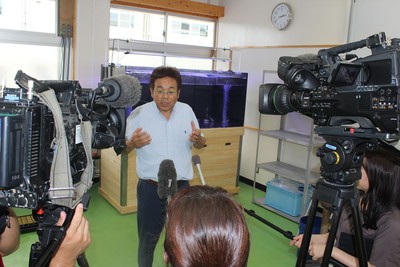 大型水槽前で報道陣の取材に答える山本准教授