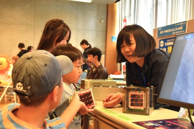 超小型人工衛星の模型で説明する宮田准教授(右)
