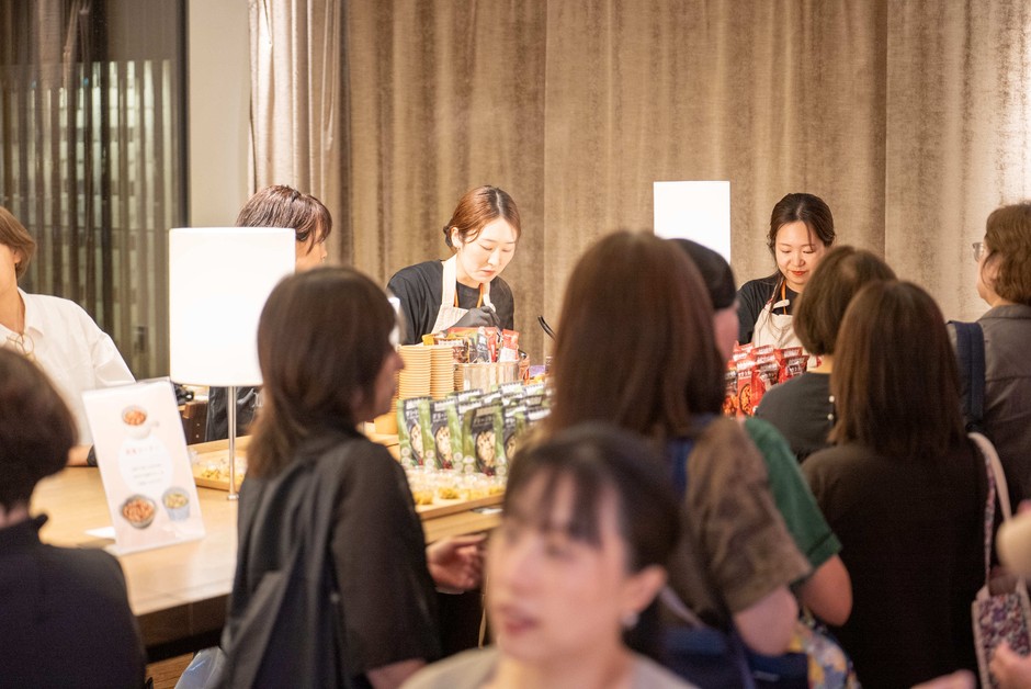 試食テーブルに集まる来場者と、料理を提供するスタッフ