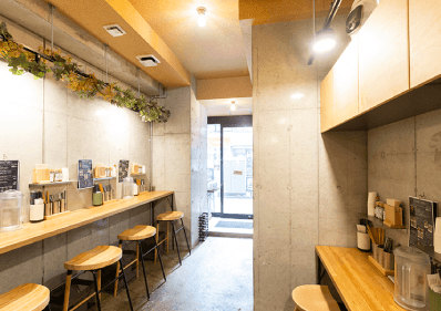 厨房を背にして店舗入口を見る。壁はコンクリート打ち放し。カフェのような雰囲気の清潔な店内