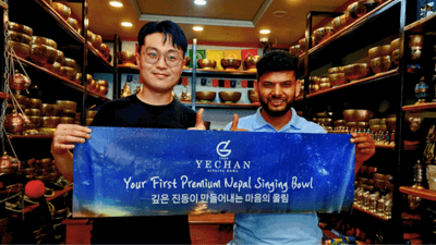 ネパールのシンギングボウル専門店で、YECHAN代表（左）と現地関係者がブランドバナーを掲げる様子